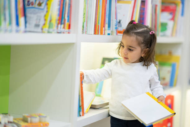 istock Little girl chooses a book in the library 1208573997