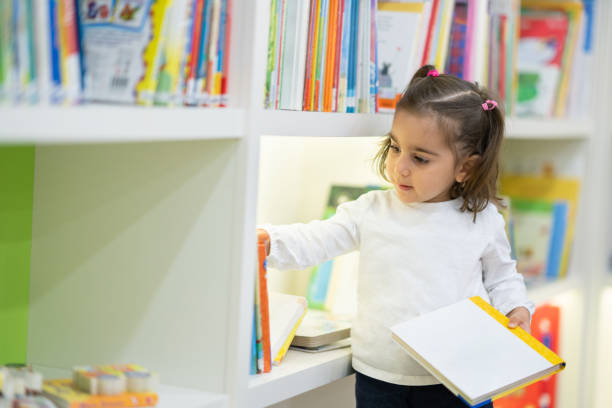 garotinha escolhe um livro na biblioteca - picture book library preschool bookshelf - fotografias e filmes do acervo