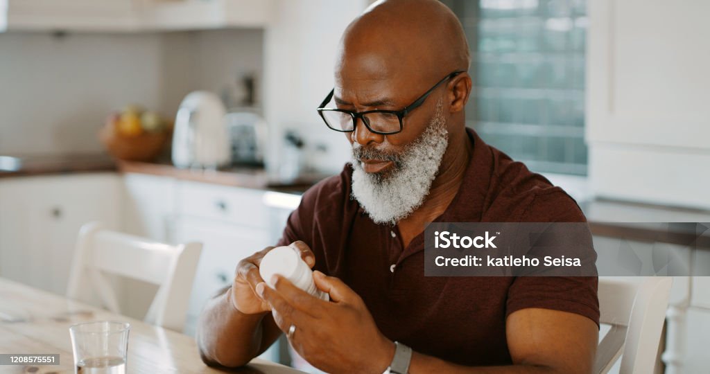 How many do I need to take? Cropped shot of a senior man sitting alone in his kitchen and taking pills Medicine Stock Photo