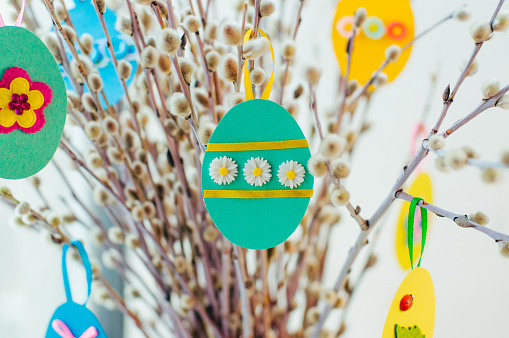 Easter eggs cutted from color paper decorated with ribbon and buttons on willow branches. Idea for DIY decoration with children.