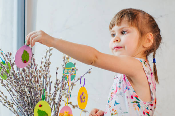 linda garotinha pendurando ovos de páscoa cortados de papel colorido - child easter egg home improvement easter - fotografias e filmes do acervo