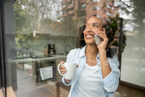 Happy African American woman at home talking on the phone while drinking a cup of coffee - lifestyle concepts