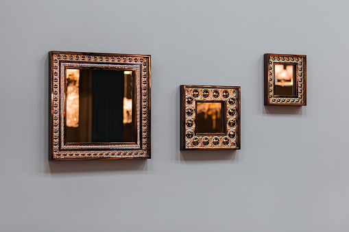 Three mirror frames on grey wall. Triptych scenery frames mirrored golden copper color.