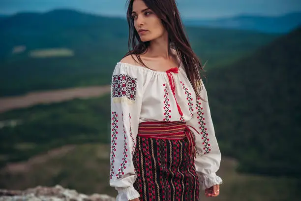 Photo of Atractive woman in traditional romanian costume on mountain green blurred background. Outdoor photo. Traditions and cultural diversity