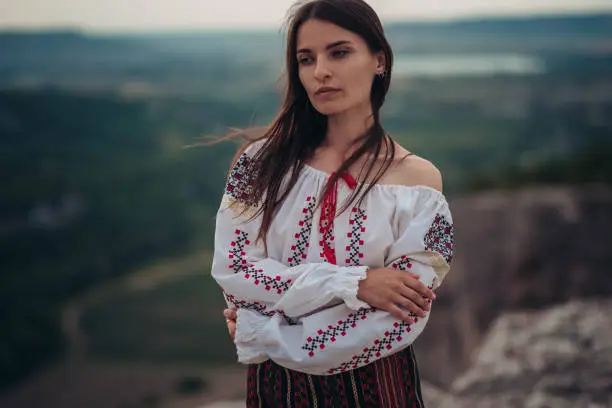 Photo of Atractive woman in traditional romanian costume on mountain green blurred background. Outdoor photo. Traditions and cultural diversity