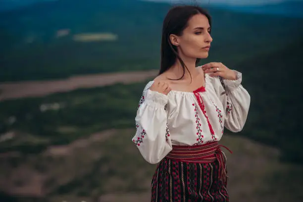 Photo of Atractive woman in traditional romanian costume on mountain green blurred background. Outdoor photo. Traditions and cultural diversity