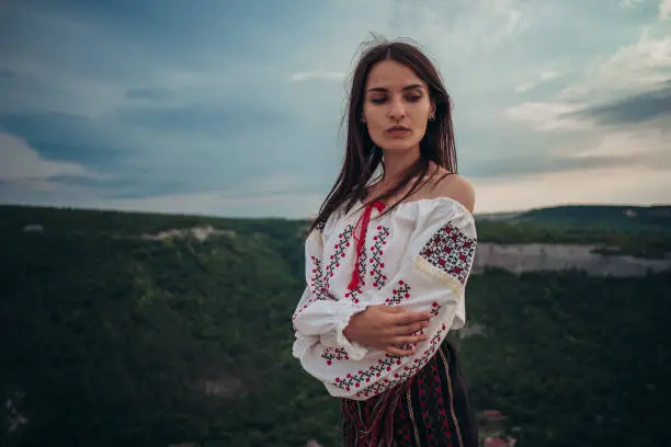 Photo of Atractive woman in traditional romanian costume on mountain green blurred background. Outdoor photo. Traditions and cultural diversity