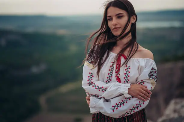 Photo of Atractive woman in traditional romanian costume on mountain green blurred background. Outdoor photo. Traditions and cultural diversity