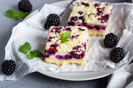 Cheesecake bars with blackberries and streusel with mint leaves on a white baking paper.