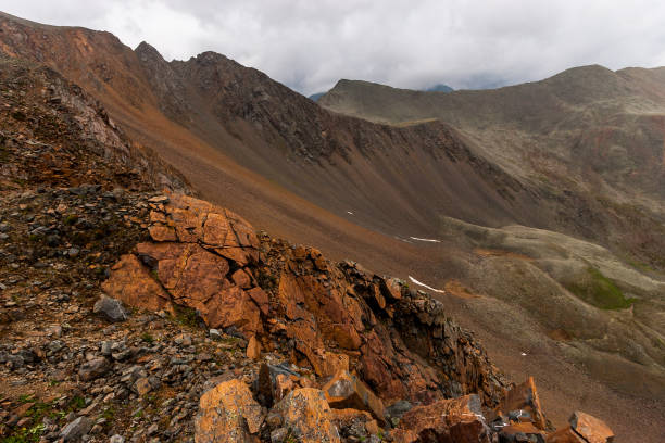 istock View from a steep cliff and a mountain range with clouds above it. Red cracked stones in the foreground. Horizontal. 1208587965