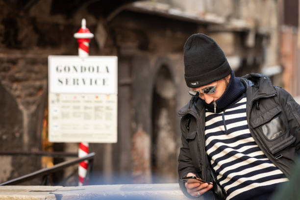 Venice, Italy - February 03, 2020: A gondoliere in Venice (Italy) waiting for customers, looking on his smartphone