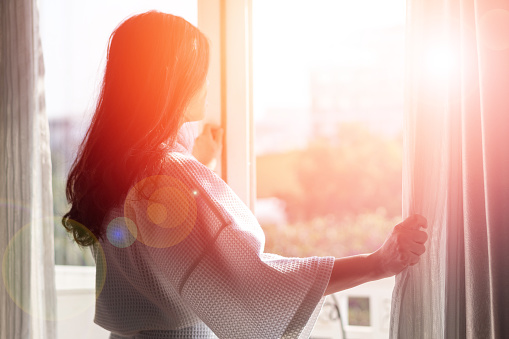 Relax business woman lifestyle at home sitting on modern chair in living room looking out of window toward beautiful cityscape downtown urban landscape city life w/ sunlight effect: