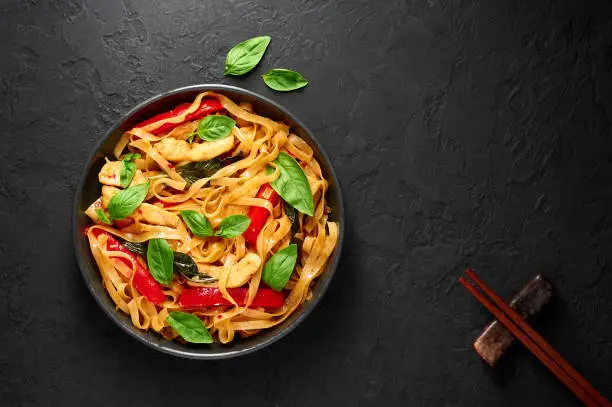 Thai Drunken Noodles or Pad Kee Mao in black bowl at dark slate background. Drunken Noodles is thai cuisine dish with Rice Noodles, Chicken meat, Basil, sauces and vegetables. Thai Food. Copy space