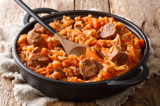braised cabbage with meat, tomatoes, carrots and onions close-up in a pan. horizontal - bigos imagens e fotografias de stock
