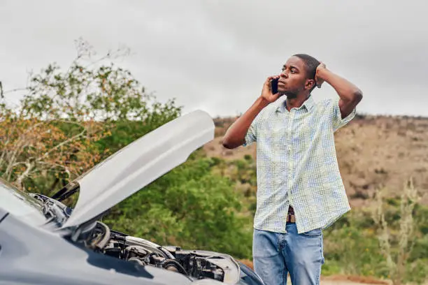 Cropped shot of a handsome young man calling roadside assistance while standing next to his broken down car outdoors