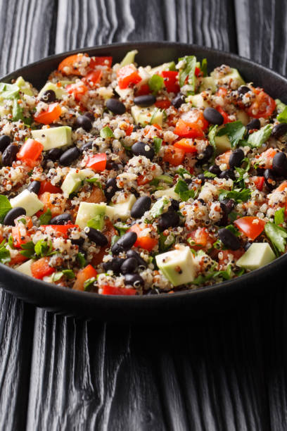 Boiled quinoa with fresh avocado, peppers, tomatoes and black beans close-up in a plate. vertical
