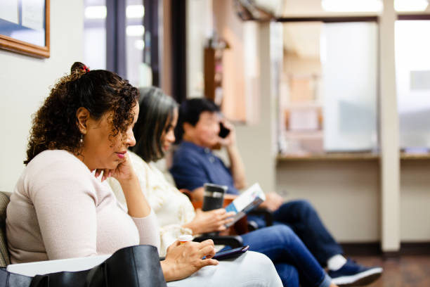 People look at brochure and use smart phones while waiting People sit in doctor's waiting room.  One woman looks a medical brochure and a man uses his smart phone to make a call. waiting room stock pictures, royalty-free photos & images