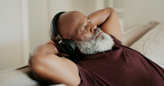 Cropped shot of a senior man sitting alone on his sofa and listening to music through headphones