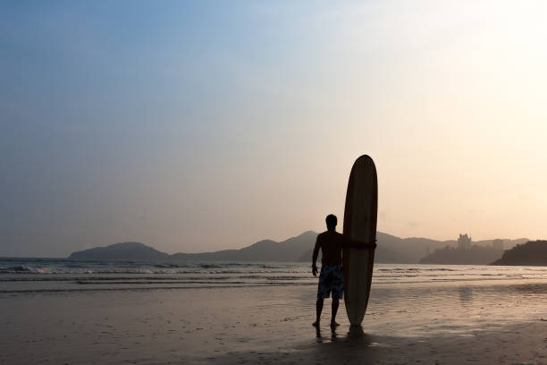 Surfer standing by the sea watching the waves
