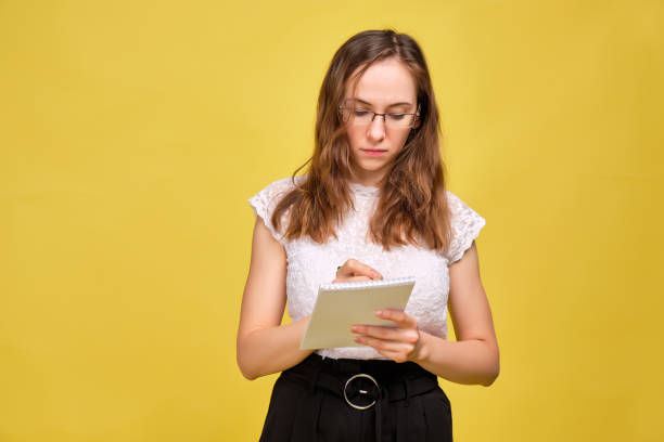 istock A girl in casual clothes and glasses on a yellow background makes notes in a notebook. Business woman concept. 1208604981