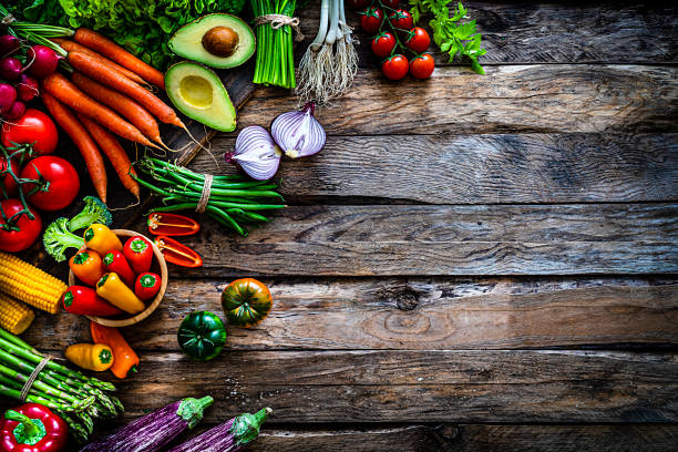 Top view of a large assortment of healthy fresh organic vegetables arranged at the left of an horizontal frame leaving useful copy space for text and/or logo at the right of an old brown wooden table. The composition includes carrots, onion, tomatoes, green beans, celery, avocado, corn, eggplant, asparagus, broccoli, bell pepper, lettuce and radish.  High resolution 42Mp studio digital capture taken with SONY A7rII and Zeiss Batis 40mm F2.0 CF lens