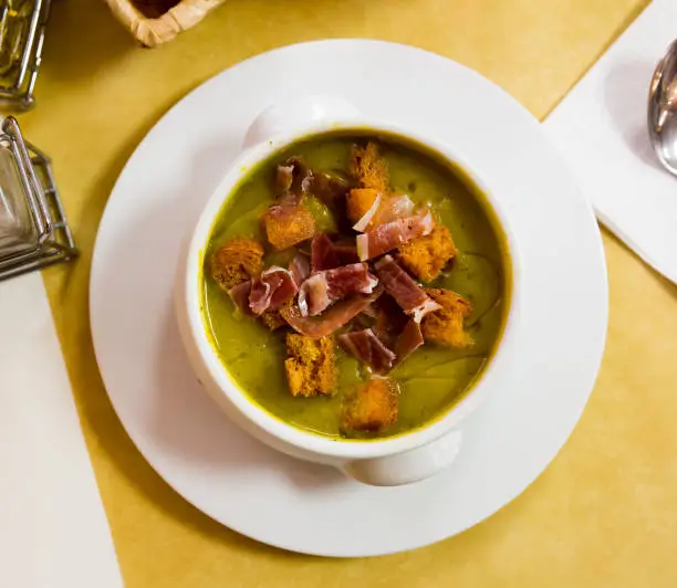 Photo of Top view of creamy zucchini soup with croutons and jamon