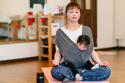 A mother is practicing yoga and meditating while carrying her baby in a baby carriage.