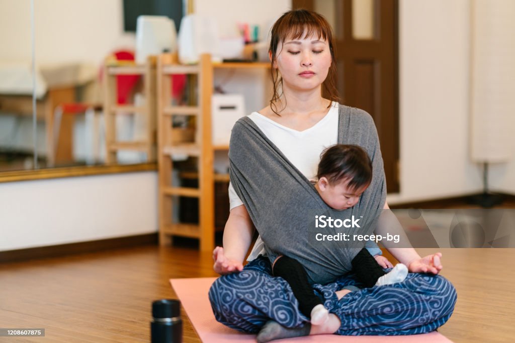 Mother doing yoga with her baby A mother is practicing yoga and meditating while carrying her baby in a baby carriage. Baby - Human Age Stock Photo
