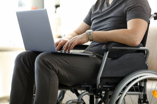 istock Man sitting in wheelchair working with laptop computer 1208610574