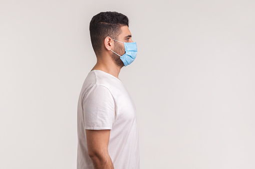 Side view of man wearing hygienic mask to prevent infection, respiratory illnesses such as flu, 2019-nCoV. indoor studio shot isolated, copy space for advertise about coronavirus prevention awareness