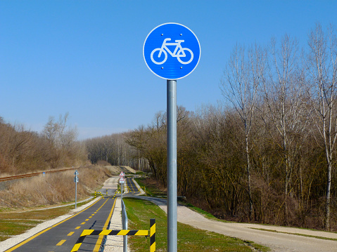 selective focus on blue traffic sign. circular metal bicycle route road and traffic sign with white bicycle symbol on aluminum post. paved asphalt path in diminishing perspective. spring nature scene
