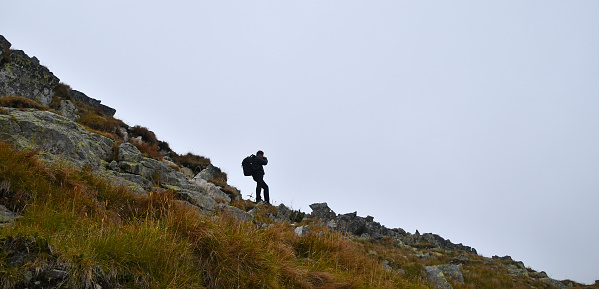 One tourist man photographer with backpack taking pictures in mountains on foggy weather day, low angle side view