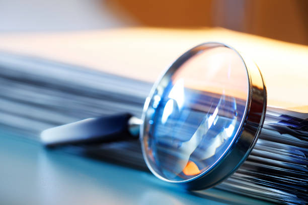 Magnifying Glass Leaning Against Stack Of Papers A magnifying glass leans against a thick stack of papers. Photographed with a very shallow depth of field. archives photos stock pictures, royalty-free photos & images