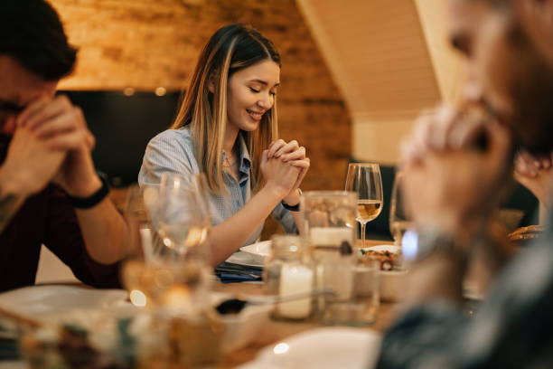 istock Smiling woman say grace while having dinner with friends in dining room. 1208623940