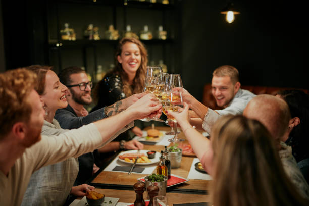 istock Best friends sitting in restaurant for dinner and making a toast with white wine. On table is food. 1208625024