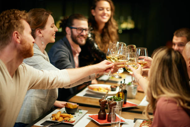 istock Best friends sitting in restaurant for dinner and making a toast with white wine. On table is food. 1208626883
