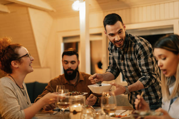 istock Happy man having fun with friends while serving them food at dining table. 1208628187