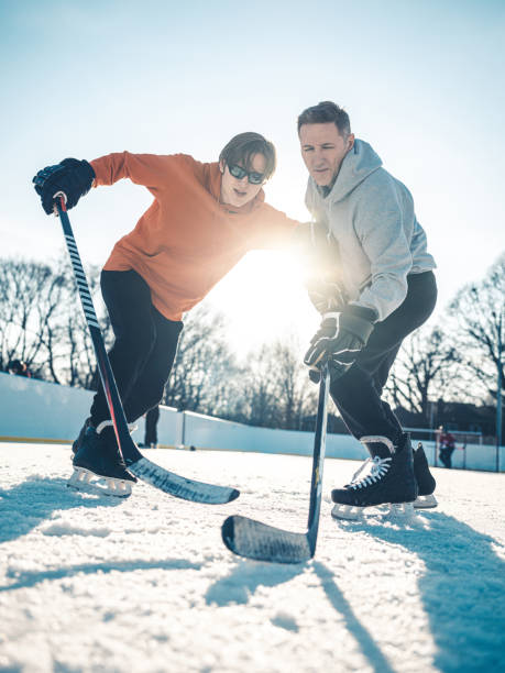 Father and son playing hockey outdoors Father and son playing hockey "one on one" at outdoor ice hockey rink in public park. checking ice hockey stock pictures, royalty-free photos & images
