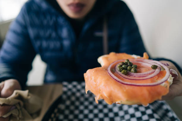 Taken in a restaurant, a person is  holding her salmon bagel in Canmore.