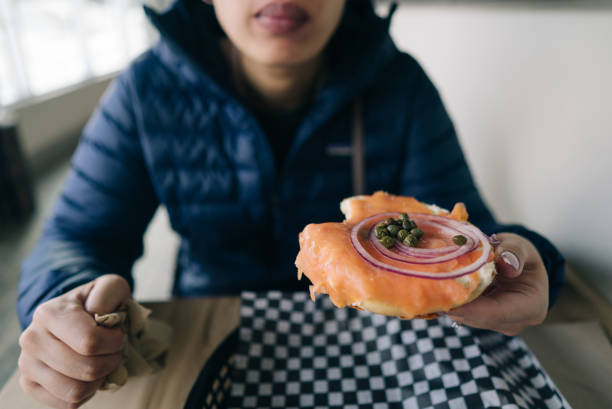 Taken in a restaurant, a person is  holding her salmon bagel in Canmore.