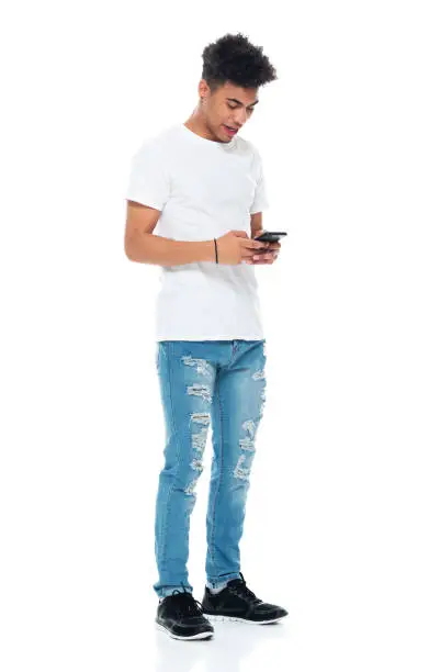 Photo of African-american ethnicity boys standing in front of white background wearing t-shirt and using smart phone