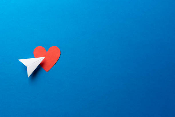 istock Paper airplane with red heart shape on blue background with space for text. Sharing and send symbol concept. Airplane flight transport sign. Landing page concept. 1208651461