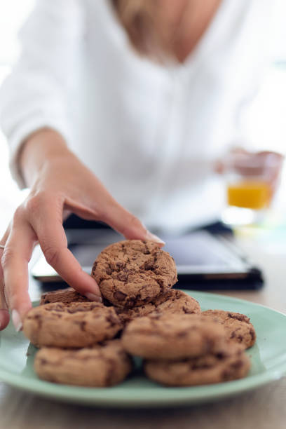 istock A woman's hand taking chocolate cookies from a plate while holding an orange juice in the other hand. 1208651823
