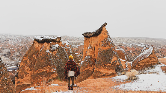 Girl walking around Fairy chimneys surronded by snow in Imaginary Valley in winter season in Cappadocia.