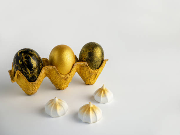 istock Easter eggs painted in gold and black in a textured stand on a white background with meringues 1208657533