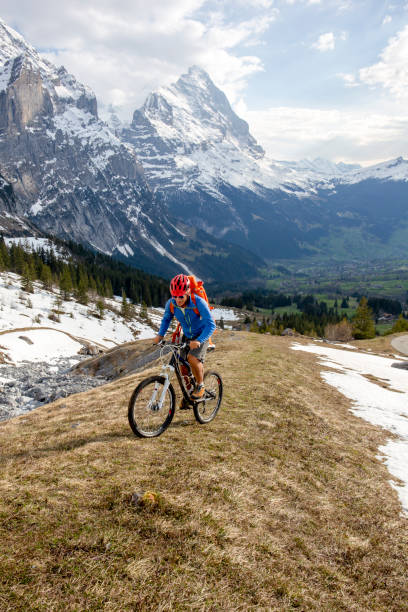 горный байкер поднимается крутой вид на склон горы айгер позади - grindelwald european alps blue sky стоковые фото и изображения