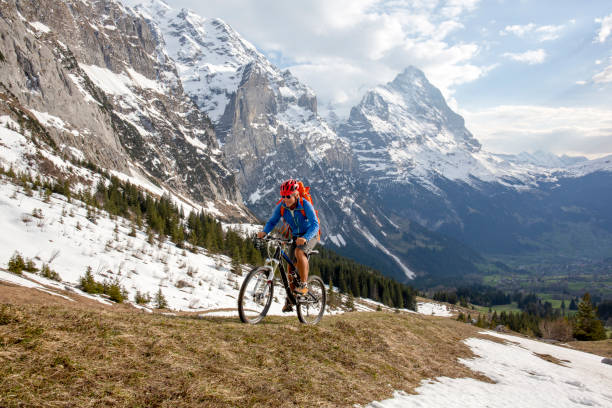 горный байкер поднимается крутой вид на склон горы айгер позади - grindelwald european alps blue sky стоковые фото и изображения