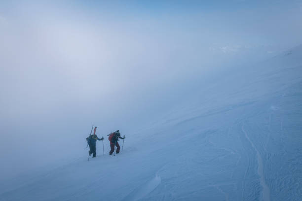 Ski mountaineers ascend snowy mountain ridge line Glaciers and more mountain ranges behind upward mobility stock pictures, royalty-free photos & images