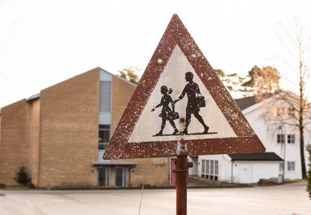 Worn school warning sign with scratches and a bullet hole.