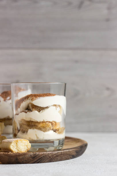 tiramisù da dessert tradizionale italiano in vetro su sfondo grigio chiaro. dolce italiano aromatizzato al caffè a base di ladyfingers e mascarpone. - tiramisu trifle italian culture dessert foto e immagini stock